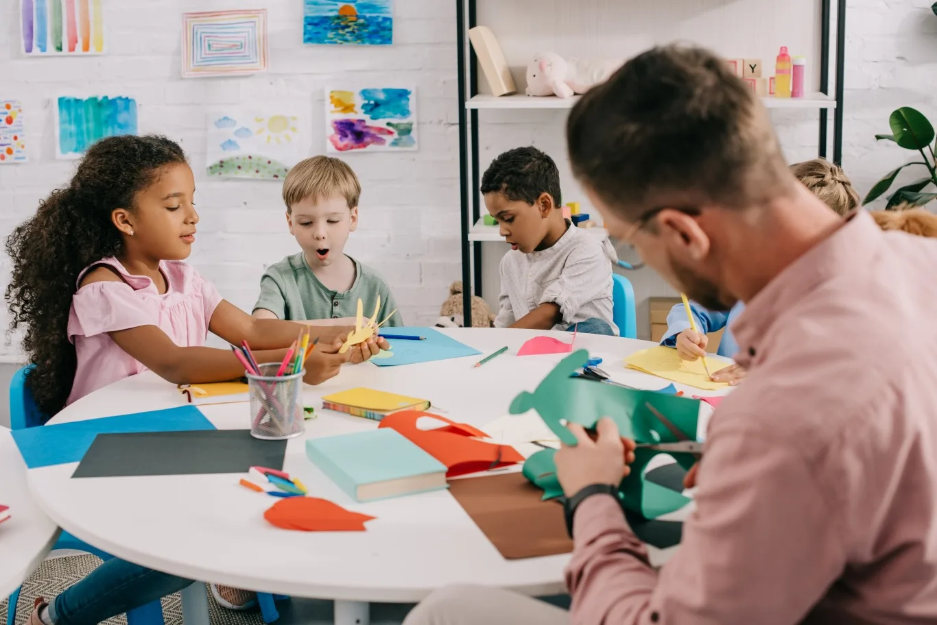 Children taking part in a creative art activity with a caregiver as part of a daycare daily routine, encouraging learning, focus, and social interaction in a supportive classroom setting.