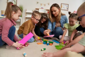 Educator guiding young children during a hands-on activity focused on play based learning, encouraging creativity, problem-solving, and social development in a supportive classroom environment.