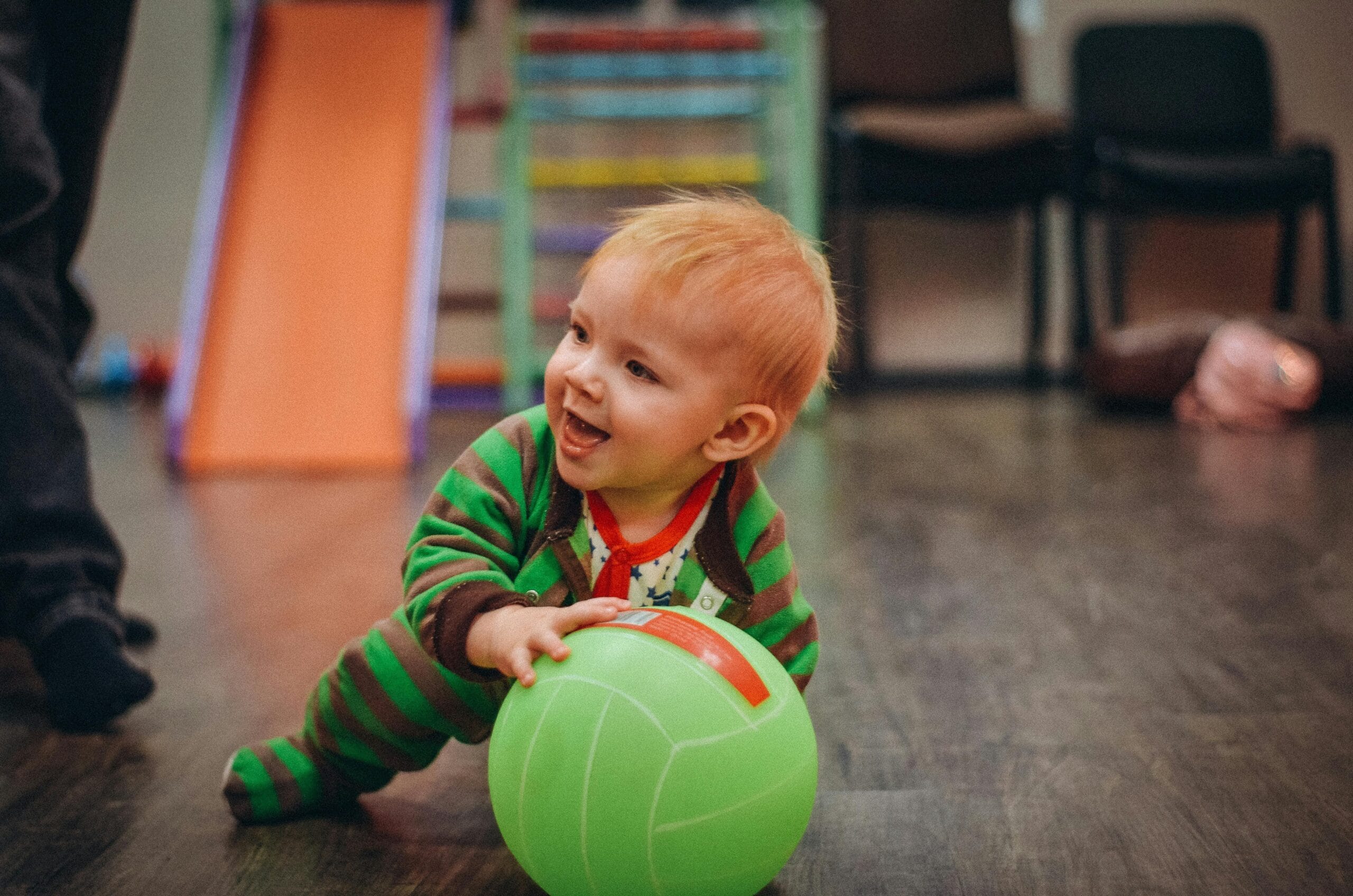 A happy infant playing with a soft ball on the floor, enjoying simple infant activities for daycare that support movement, coordination, and early sensory development.