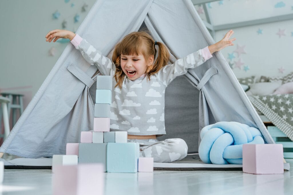 Toddler playing with colourful blocks inside a small indoor play tent, demonstrating play based learning through creative building and imaginative exploration.