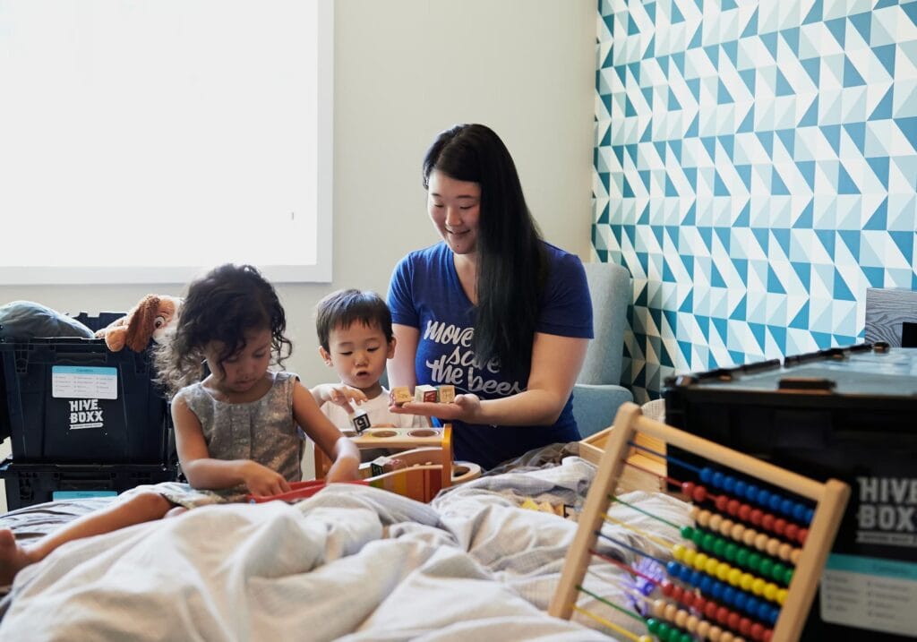 A caregiver engaging young children in hands-on learning activities with toys and blocks, showcasing a warm and interactive kiddie daycare environment that supports early development.