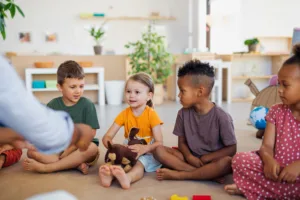 Two young children smiling and playing cooperatively with natural wooden building blocks inside a bright, spacious room at a licensed day care in langley, showcasing a high-quality early childhood learning environment.